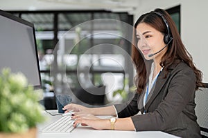 A professional Asian female call centre operator with a headset is working at her desk