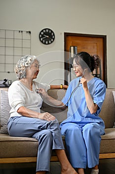 Professional Asian female doctor visiting her retire female patient at home, checking heart beat`s