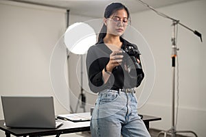 Professional Asian female photographer is focusing on adjusting her DSLR camera, working in a studio