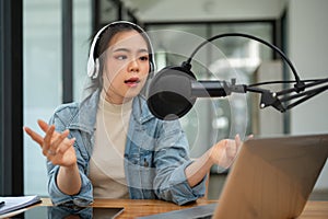 A professional Asian female radio host or podcaster is speaking into a microphone