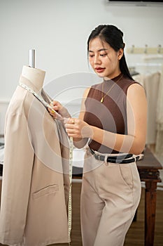 A professional Asian female tailor is working in her studio, measuring sizes with a measuring tape