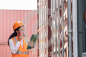 Professional asian female workerusing walkie-talkie in shipping yard industrial container box from cargo freight ship for import