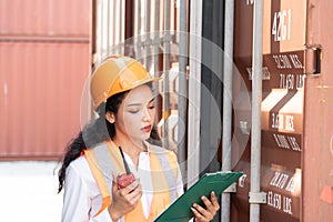 Professional asian female workerusing walkie-talkie in shipping yard industrial container box from cargo freight ship for import