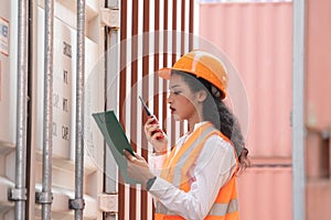 Professional asian female workerusing walkie-talkie in shipping yard industrial container box from cargo freight ship for import