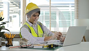 Professional Asian male architect using laptop computer, working on construction plan at his workplace