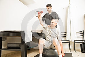 Professional Assisting Patient In Lifting Weights In Physiotherapy Clinic