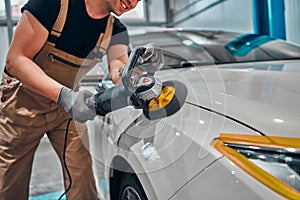 Professional auto detailer hand holding rotary polisher while polishing paint surface of shiny white car