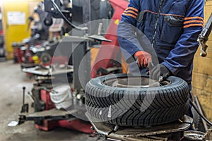 Professional auto mechanic replacing tire on wheel in car repair service.