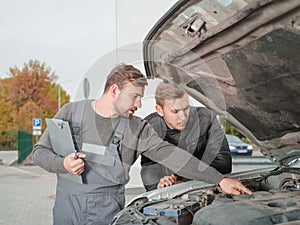 Professional auto mechanic showing something in the open hood to client outside.