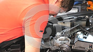 Professional auto mechanic works under hood of vehicle. Repairman fixing engine of a car at workshop or service. Man