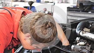 Professional auto mechanic works under hood of vehicle. Repairman fixing engine of a car at workshop or service. Man