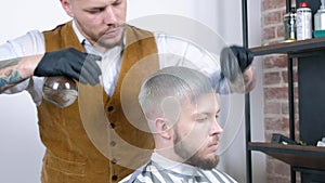 A professional baber working a hairstyle combing it with water. male client with blond hair.