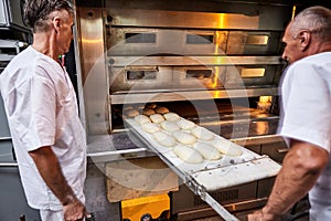 Professional baker in uniform inserts cart with decks for baking raw dough to make bread in an industrial oven in a bakery