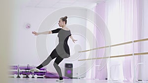 A professional ballerina in a black pack dances in a large training hall