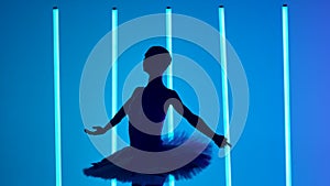 Professional ballerina is dancing ballet and performing graceful jumps in a dark studio. Silhouette of young girl in a