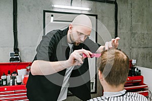 Professional barber cuts the client with scissors and a comb with a serious face. Male hairdresser creates stylish haircut for