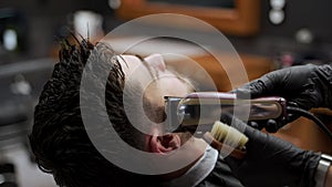 Professional barber gives stylish haircut with electric clipper at modern barbershop. Male client getting trim, fade