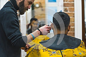 Professional barber gromming his client& x27;s hair in a barbershop. Back view of client& x27;s head. Mirror in the
