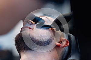 Professional barber shaves customer beard with straight razor