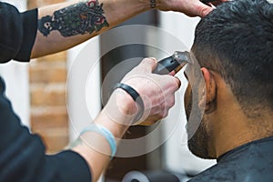 Professional barber with tattoos gromming his client& x27;s hair with electric trimmer in a barbershop.