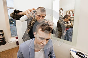 Professional barber using hairspray on male customer in shop