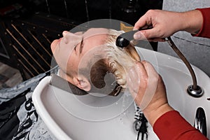 A professional barber washes white dye young guy's client's hair sink painting barbershop