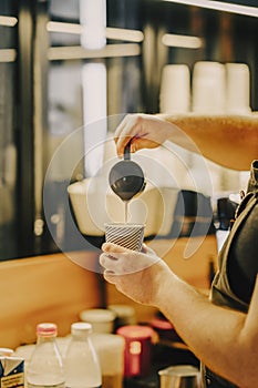 Professional barista hands pouring steamed milk into coffee paper cup, making cappuccino