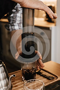 Professional barista preparing coffee in aeropress, alternative coffee brewing method. Hands on aeropress and glass cup, scales,