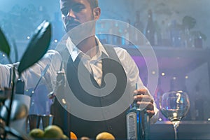 Professional barman in a white shirt and black apron making cocktail at party in a tropical nightclub. Nightlife concept