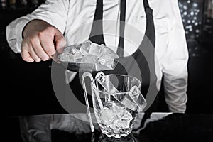 A professional bartender adds cold ice cubes on a scap to a serving dish