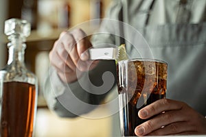 A professional bartender decorates the cocktail with lime. The bartender prepares a cocktail with whiskey and Cola