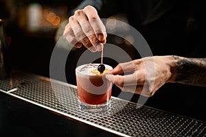 Professional bartender decorating a pink alcoholic cocktail in the glass with a dried orange and a berry on the