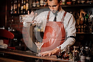 Professional bartender pourring cocktail with an ice cubes into