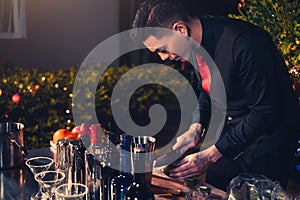 Professional bartender preparing fresh lime lemonade cocktail in drinking wine glass with ice at night bar clubbing counter.