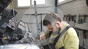 Professional bearded repairman fixing car with open hood at workshop. Auto mechanic in uniform working with vehicle at