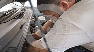 Professional bearded repairman with wrench fixing engine of a car at workshop. Auto mechanic in uniform working under