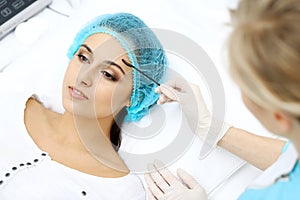 Professional beautician is doing cosmetic procedure at light medical background touching patient`s face with brush