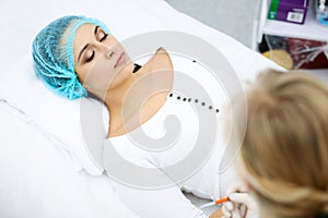 Professional beautician is doing cosmetic procedure at light medical background touching patient`s face with brush