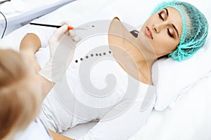 Professional beautician is doing cosmetic procedure at light medical background touching patient`s face with brush