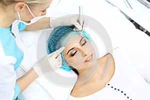 Professional beautician doing eyebrow tattoo at woman face. Permanent brow makeup in beauty salon, closeup. Cosmetolog