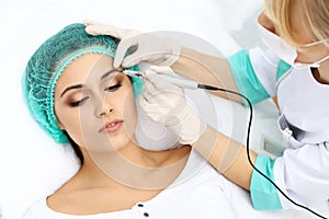 Professional beautician doing eyebrow tattoo at woman face. Permanent brow makeup in beauty salon, closeup. Cosmetolog