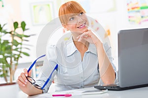 Professional beautiful young woman sitting her desk an holding glasses in her hands