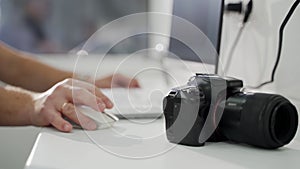 Professional black camera on desk, photographer's hands working with computer, uploading photo at the office. Modern