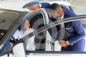 Professional Black Manager In Auto Showroom Consulting Female Client Sitting In Car