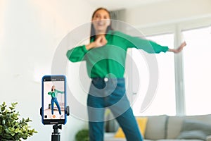 Professional blogging concept. Joyful female blogger making video via smartphone, dancing and recording content at home