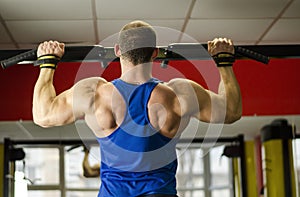 Professional bodybuilder with ideal muscular body doing pull-ups in the gym