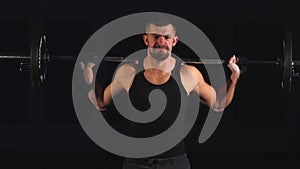 Professional bodybuilder workout with barbell on black background. Muscular man training squats with barbells over head