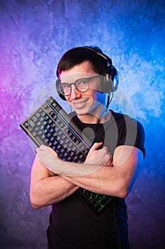 Professional Boy Gamer holding gaming keyboard over colorful pink and blue neon lit wall. Gaming gamers concept