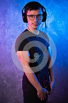 Professional Boy Gamer holding gaming keyboard over colorful pink and blue neon lit wall. Gaming gamers concept