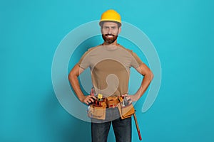 Professional builder in hard hat with tool belt on light blue background